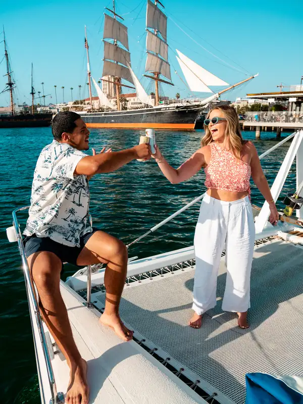 Wedding couple toasting aboard Malarky with a historic tall ship behind on San Diego Bay